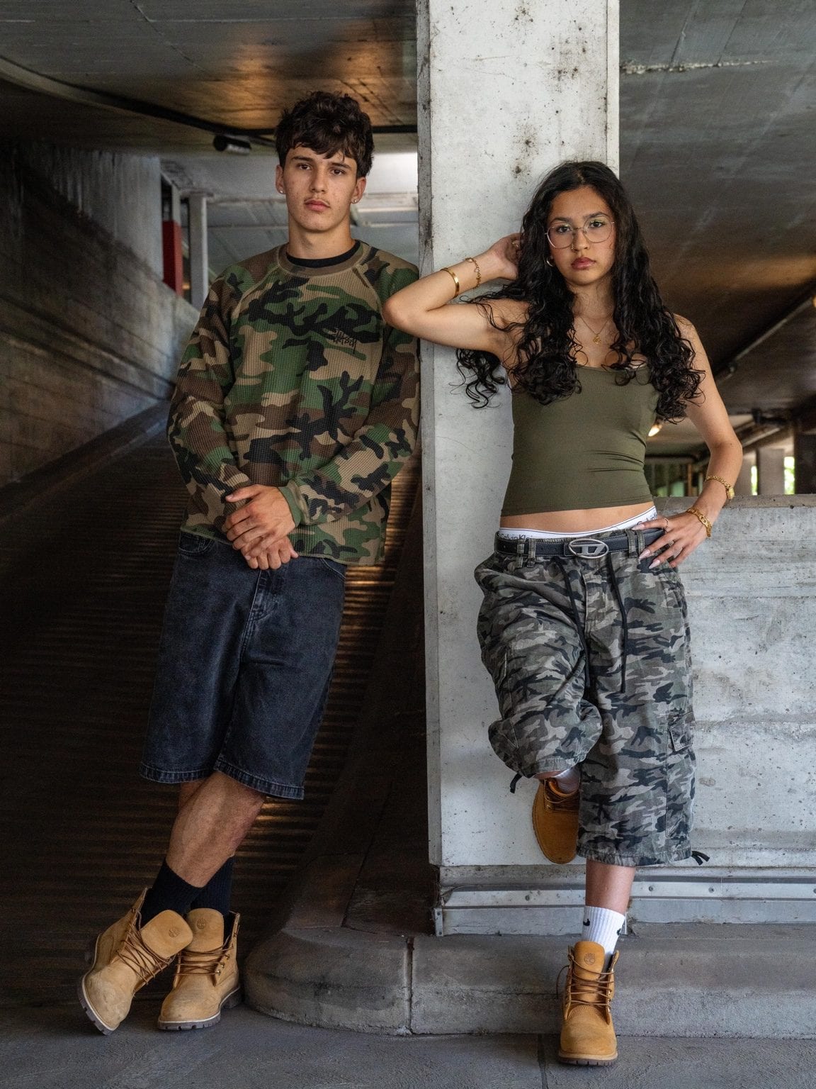 Le couple debout contre un pilier en béton sous un passage couvert, en tenues camouflage assorties