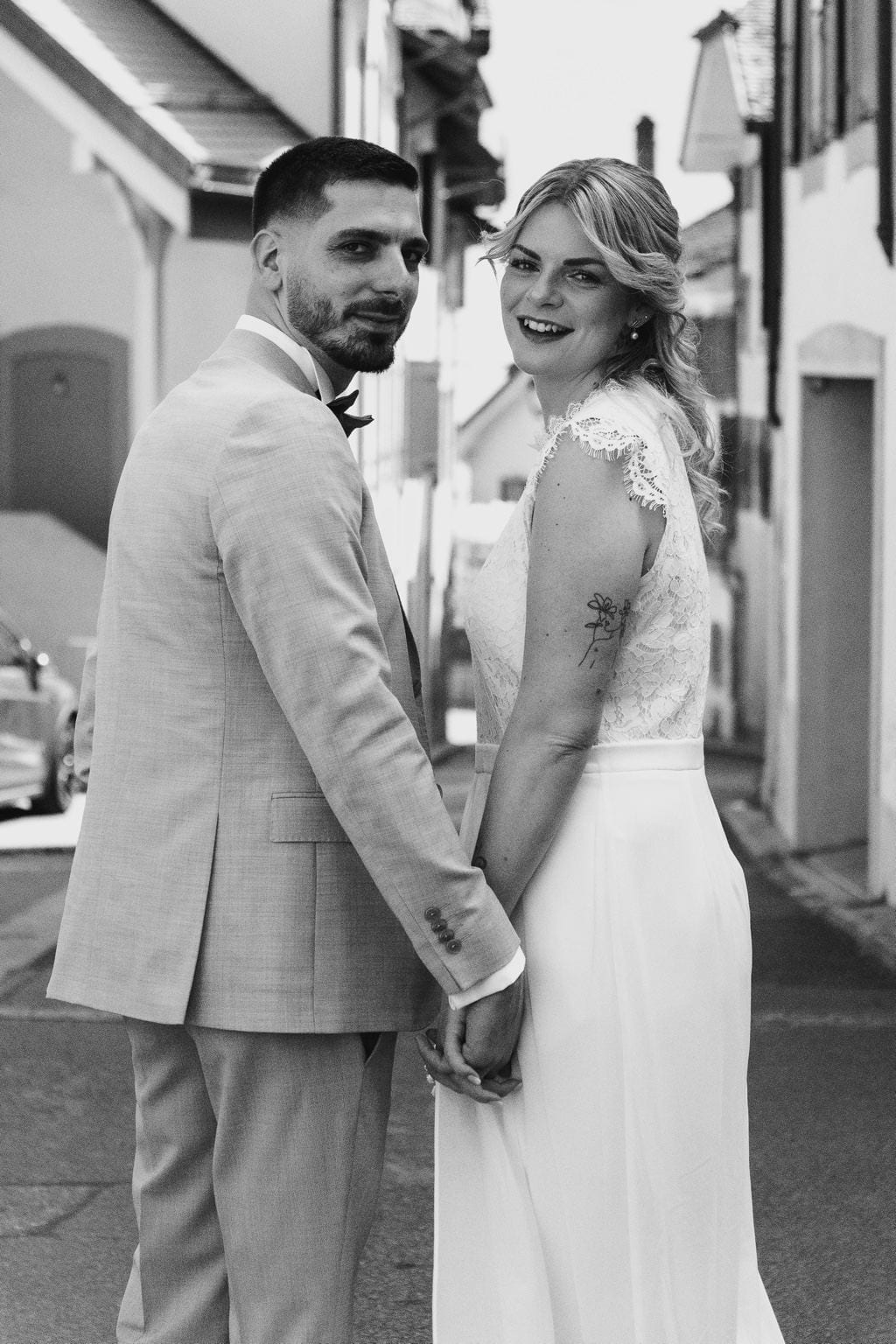 Kenza et Steven main dans la main dans une ruelle, se retournant vers l'objectif, en noir et blanc