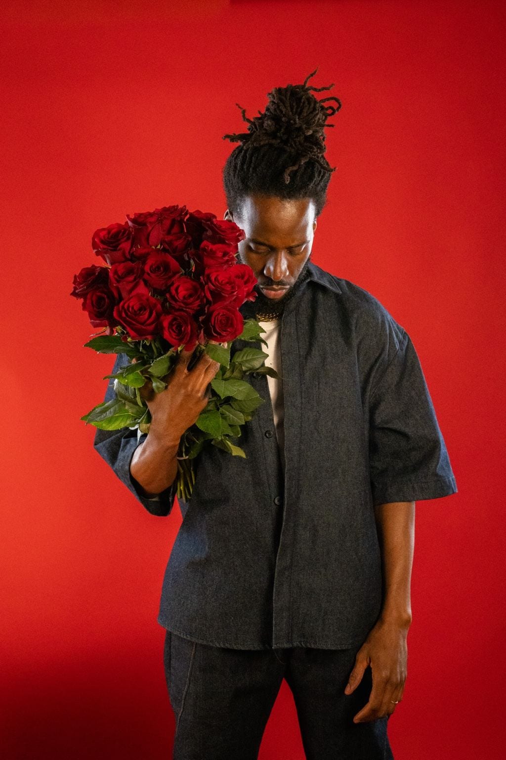 Jules en chemise sombre, le visage penché sur un bouquet de roses rouges, sur fond rouge en studio