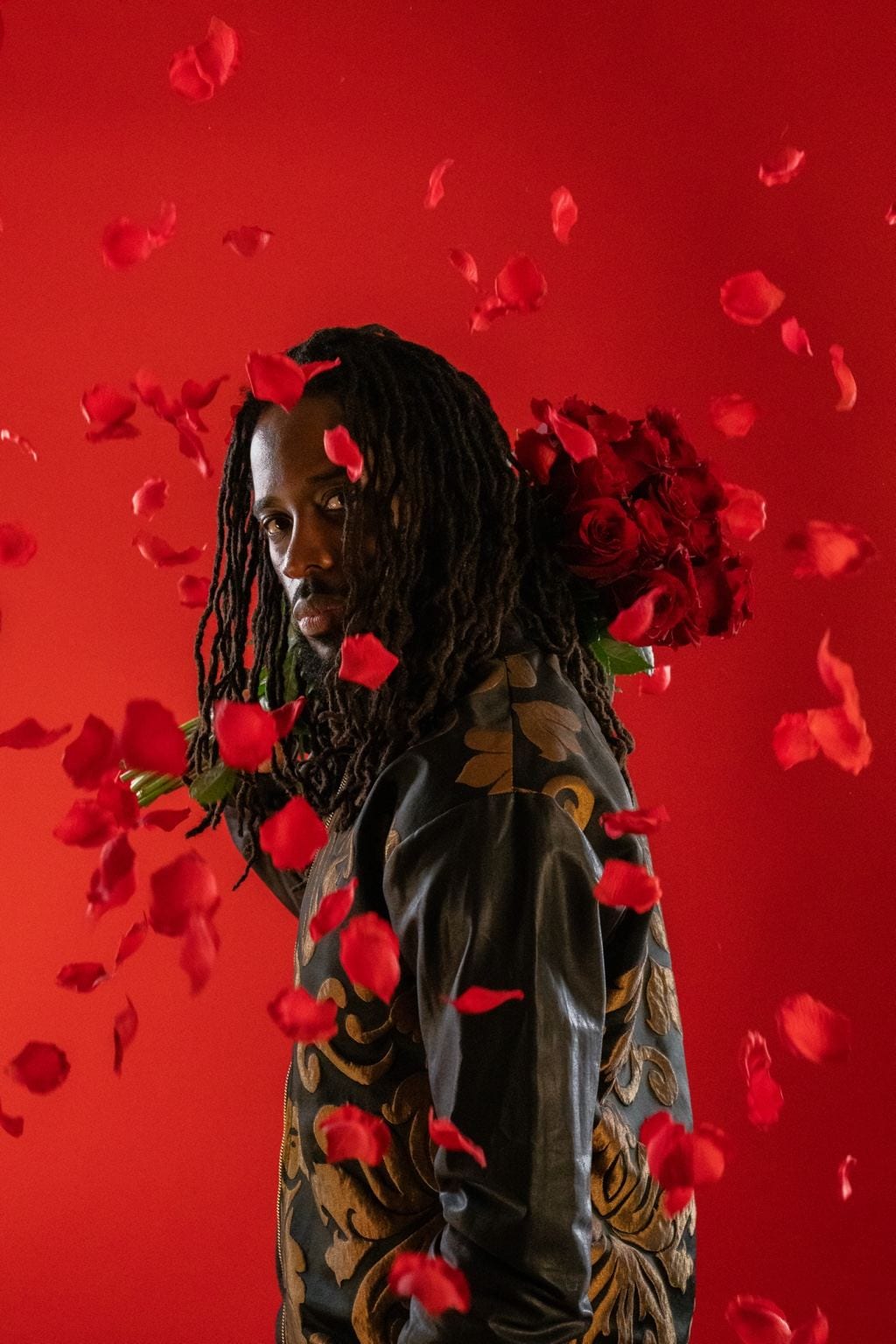 Jules devant un fond rouge, un bouquet de roses rouges à l’épaule, des pétales en suspension